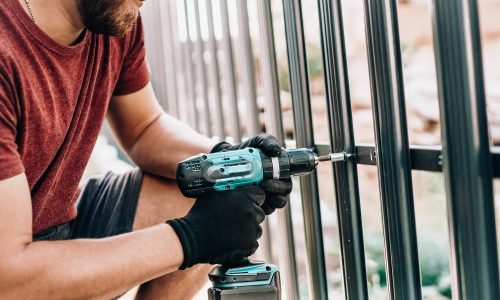 Close up portrait and details of caucasian male worker using screwdriver and screwing metal fence