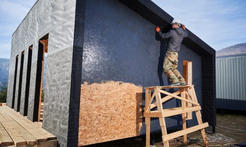 Male painter using paint roller, doing exterior paint work while building wooden frame house.