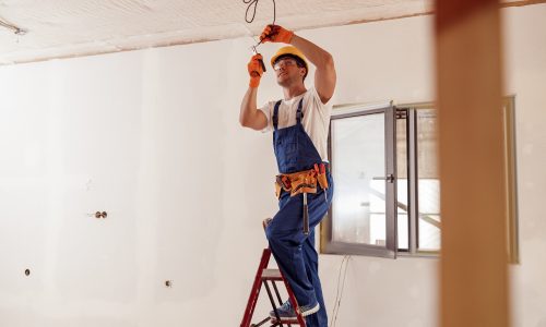 Smiling electrician fixing electric cable on ceiling